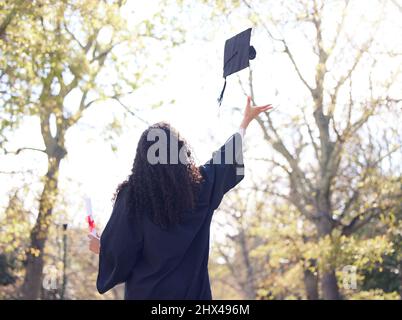 A bright future is about to begin. Rearview shot of a young woman throwing her cap in the air on graduation day. Stock Photo