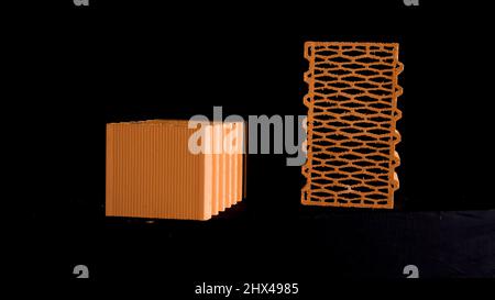Wall construction materials, small pile of ceramic blocks isolated on black background. Red new perforated bricks. Stock Photo