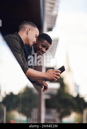 Have you seen this. Shot of two businessman looking at something on a cellphone while standing on the balcony of an office. Stock Photo