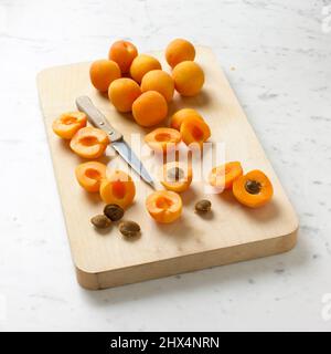 Apricots on a chopping board with a knife, stones and apricot halves. Stock Photo