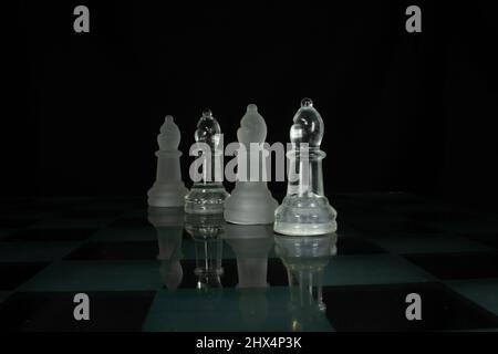 two white opaque and two clear chess piece bishop isolated on a chequered chess board with a black background Stock Photo