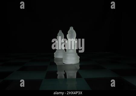 two white opaque chess piece bishop isolated on a chequered chess board with a black background Stock Photo