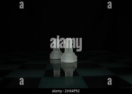 two white opaque chess piece pawns isolated on a chequered chess board with a black background Stock Photo