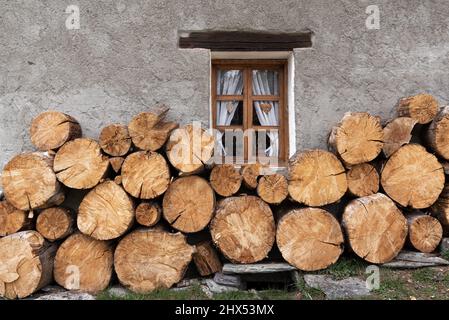 Large cut timber firewood logs stacked against the grey rendered wall of a rustic farmhouse in Chamonix France Stock Photo