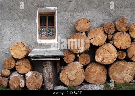 Large cut timber firewood logs stacked against the grey rendered wall of a rustic farmhouse in Chamonix France Stock Photo
