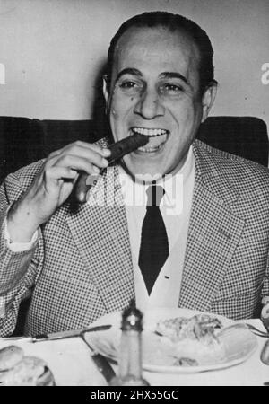 Even Crooners Must Eat -- So France's popular Tino Rossi gets down to a meal of sausages and potato salad in Berlin, where he received a great reception from many German fans. He is on a big tour of Germany. March 19, 1951. (Photo by Paul Popper Ltd.). Stock Photo