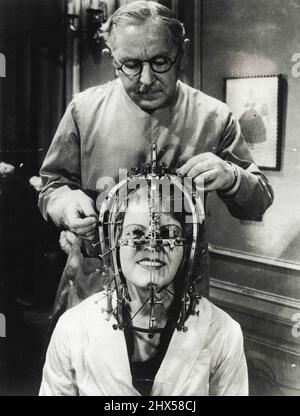 A Beauty Michrometer This 'Beauty Michrometer' was designed by Max Factor, the famous Hollywood make-up artist, who is here seen demonstrating the instrument with Miss Marjorie Reynolds. The instrument makes exact facial measurements and discloses which features should be enhanced or reduced in making-up. The device fits over the head and face, itsinnumerable flexible metal strips fitting to the various features and then being held in place by set screws. There are 325 adjustment possible on the instrument. October 29, 1934. (Photo by Keystone). Stock Photo