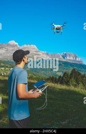 Young man flying drone on amazing mountain landscape. Man operating a drone with remote control taking aerial photos and videos. Stock Photo