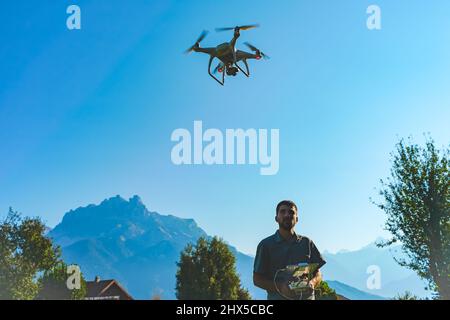 Young man flying drone on amazing mountain landscape. Man operating a drone with remote control taking aerial photos and videos. Stock Photo