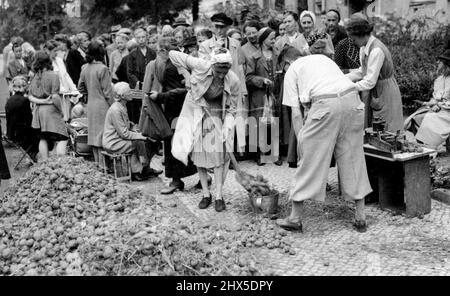 No Holidays For The Germans - German civilians Queuing for their ration of potatoes in Berlin. One woman is seen shovelling them into baskets, buckets and other Receptables for weighing. While English seaside resorts are catering for record August Bank Holiday crowds in many instances exceeding the pre-war desperately Grappling with their food problems. August 20, 1945. (Photo by Associated Press Photo). Stock Photo