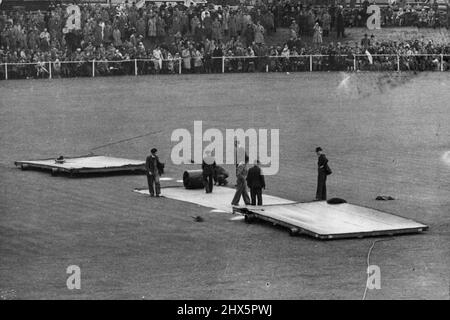 Ground staff at via Trafford worked frantica in a big mopping up operation, hoping that the rain would stop. Play was abandoned for the day this afternoon on the opening day of the Australian cricket team's three-day match against Lancashire. August 02, 1948. (Photo by Sport & General Press Agency, Limited). Stock Photo