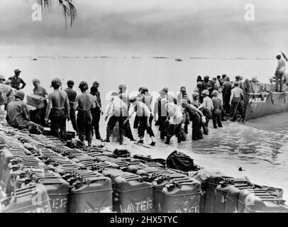 Bucket Brigade - These Marines line up, on the beach on Saipan Island, to speed the unloading of supplies and water cane. Row on row of cans filled with much needed water await transportation to interior. U. S. ships and landing craft stand by to bring in supplies, and safeguard beach. July 13, 1944. (Photo by Official U. S. Marine Corps Photograph) Stock Photo