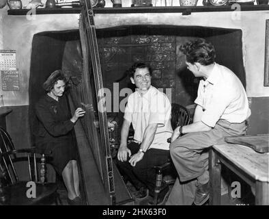 No Wonder He's Laughing --A real old piece of Wakes finds its place on the ser of the Dolwyn Arms in 'The Last Days of Dolway,' directed by Emlyn Williams at Isleworth Studios. In the old days every welsh inn had its harp and harpist. In this case, the harpist is Nancy Richards who records some of the traditional Welsh music to the beard in the film. The harp is one of the only two remaining traditional, three stringed instruments in existence. Enjoying Emlyn's delight is his Associate Director Stock Photo