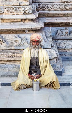 Sadhu sitting cross-legged by a typical carved wall in the Jagdish Temple, a Hindu temple in Udaipur, Indian state of Rajasthan, India Stock Photo