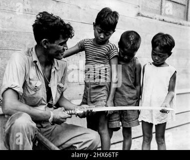 Hero Worship -- Filipino children solemnly inspect a Samurai sword that Private First Class Cornelius A. Lubo, Syracuse, New York, took from a Jap officer after slaying him and his sixteen-man patrol at Palo Bridge, Palo, Leyte Island. December 11, 1944. (Photo by USA Signal Corps Photo). Stock Photo