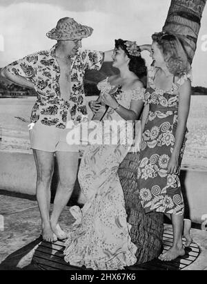 Chic Young on a visit to Hawaii to find a house for his family. He intends to draw 'Blondie' while wintering in Honolulu. With two of his fellow guests at the loyal Hawaiian Hotel, he wears a coconut hat woven from palm fronds and the typical Hawaiian 'Aloha' shirt. Young wandered far from the Bumstead suburbia when he spent a winter in Hawaii, drawing a frozen Dagwood while in the tropics. April 12, 1950. Stock Photo
