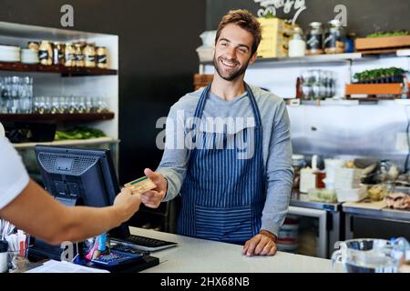 Hes got smiles for every single customer. Shot of a handsome young businessman taking payment from a customer. Stock Photo