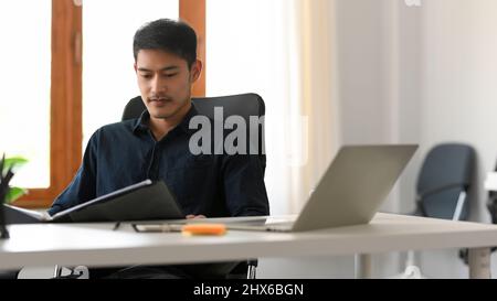 Professional and Smart Asian businessman reading and examine business report at his office desk. Stock Photo