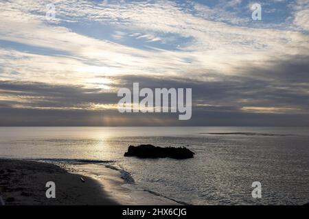 dramatic light streaming through wispy clouds over calm ocean water Stock Photo