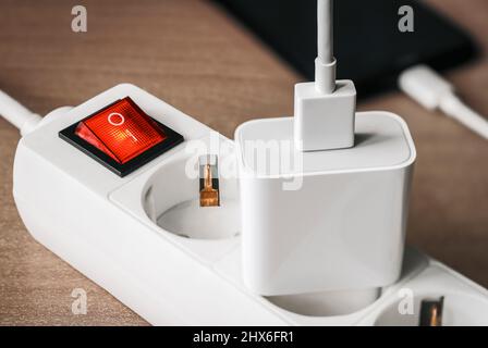 A charger adapter with a USB cable connected to a power supply with a red switch for charging a smartphone. Stock Photo