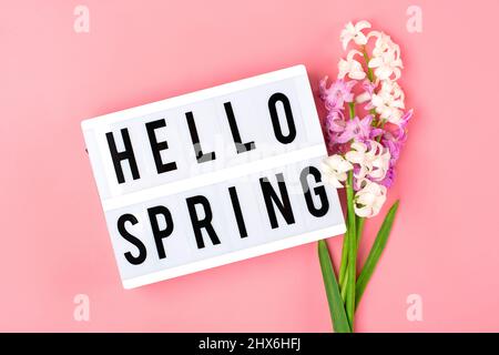 bouquet of spring flowers of lilac hyacinths, text Hello Spring on pink background Top view Flat lay Holiday card Hello spring concept Stock Photo