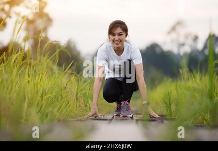 young woman in starting position ready for running on wooden path in field Stock Photo