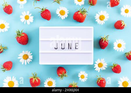 Summer month June text on light box and strawberry, chamomile flowers on blue background. Top view Flat lay. Creative concept Hello June. Top view, Fl Stock Photo