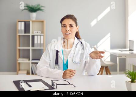 Female doctor sitting at desk and giving online consultation to patient on video call Stock Photo