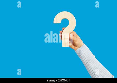 Human hand holding question mark against blank blue background for FAQ and answers Stock Photo