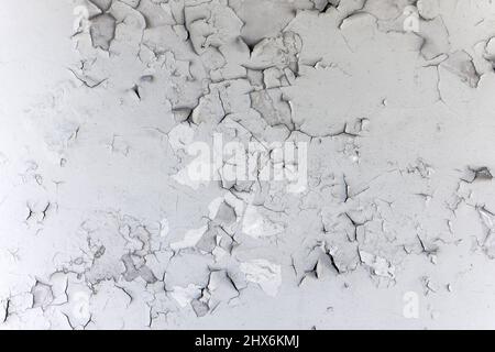 Old white paint exfoliates with cracked layers on the wall of concrete Stock Photo