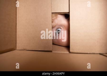 Child open carton delivery box, packaging open and closed cardboard box. Close up eyes looking. Child boy looking surprised into a gift. Stock Photo