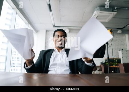 Close-up low-angle view of angry African American business man throwing up paper account documents scream shout. Stock Photo