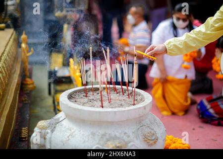 Close focus on lady hand light candle and incense on big jar with blurry background of unknown people come to worship buddha stupa inside sacred pagod Stock Photo