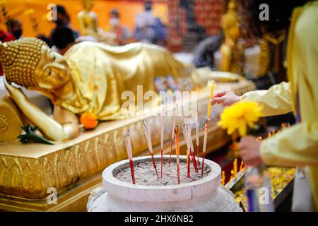 Close focus on lady hand light candle and incense on big jar to worship buddha stupa inside sacred pagoda with blurry background of golden buddha in s Stock Photo