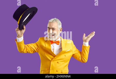 Happy cheerful senior man in yellow suit greets you and takes off his black top hat Stock Photo
