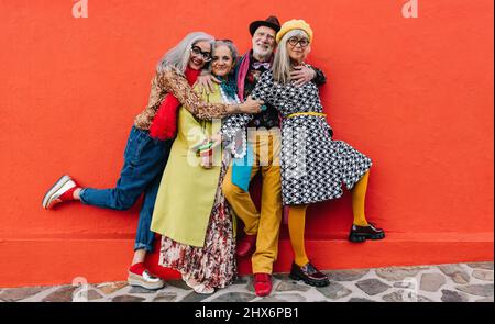 Four happy senior citizens having a good time while standing together against a red background. Group of cheerful elderly friends celebrating their re Stock Photo