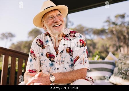 Enjoying life after retirement. Happy elderly man looking away cheerfully while sitting on a couch at a luxury spa resort. Carefree senior man enjoyin Stock Photo