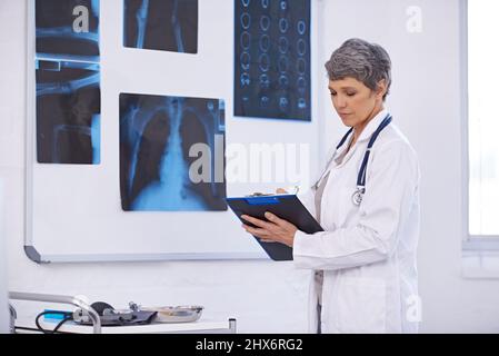 Taking down important notes from the x-rays. Shot of a female doctor studying x-rays. Stock Photo