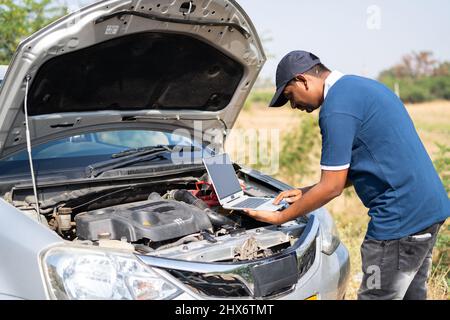 professional mechanic using laptop for checking car by lifting car hood on highway road - concept of technology, mobile repair service and support. Stock Photo