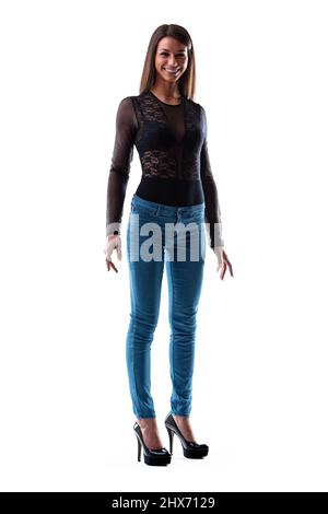 Trendy slender young woman with a vivacious smile posing full length in tight fitting jeans and high heel platform shoes isolated on white Stock Photo