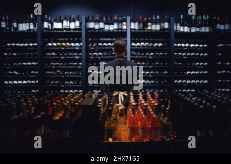 Blurred background for tasting, sommelier standing at wine shelf in liquor store. Stock Photo