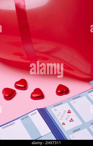 Heart-shaped candies and calendar on pink background Stock Photo