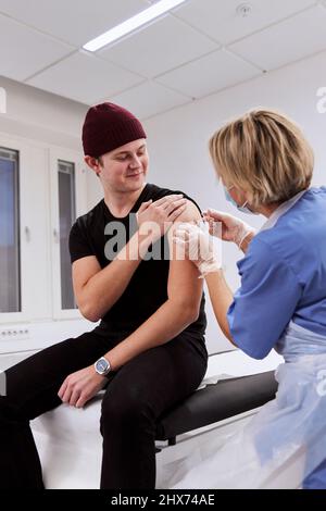 Smiling young man getting vaccinated against Covid-19 Stock Photo