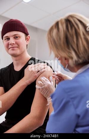 Smiling young man getting vaccinated against Covid-19 Stock Photo