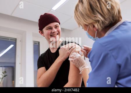 Smiling young man getting vaccinated against Covid-19 Stock Photo