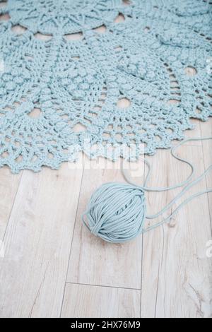 Handmade carpet knitted from natural threads, flooring, natural cotton. Beige handmade carpet. Knitted decorative item. Skein of blue knitting thread Stock Photo