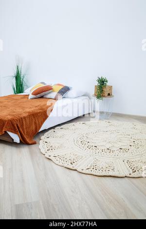 Cute homemade knitted pattern of thick threads made by hand: a handmade rug made of beige threads lies in the bedroom near the bed, the art of knittin Stock Photo