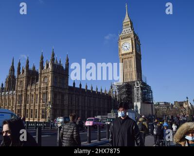 London, UK 25th February 2022. People wearing face masks walk along Westminster Bridge past the Houses of Parliament and Big Ben Stock Photo
