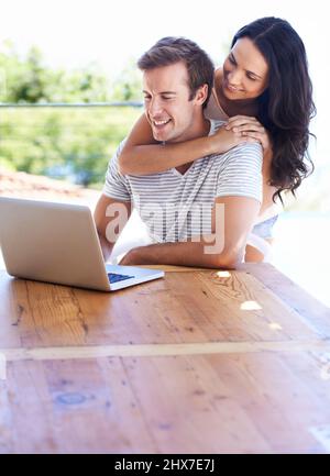 Surfing the web outside. A young couple using their laptop on the patio. Stock Photo
