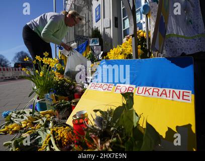 Hamburg, Germany. 10th Mar, 2022. An employee of the Consulate General of Ukraine sorts the discarded flowers and posters in front of the entrance to the consulate. Credit: Marcus Brandt/dpa/Alamy Live News Stock Photo